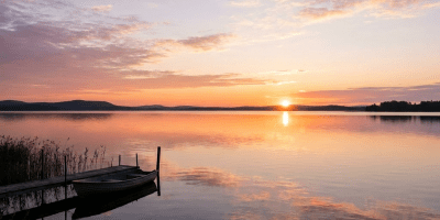 Boat tied to a wooden dock on a calm lake at sunset with reflections on the water